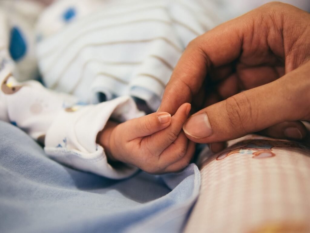 En förälders hand som håller i sin nyfödda bebis hand.